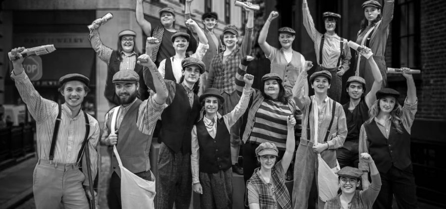 A black and white promotional image of the cast of the Actors Guild of Parkersburg's "Newsies." The people in the photo are in a large group and are dressed in turn-of-the-century clothing.