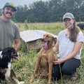 Molly Sowash and CJ Morgan with their two dogs smiling in their cow pasture.