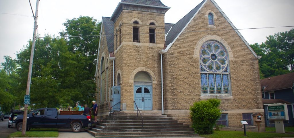 A wide shot showcases the architectural beauty of the historical Mount Zion Baptist Church. A truck is seen in front, with three pews from the church.