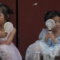 Children cool themselves with electric fans in Beijing. They are wearing princess dresses.