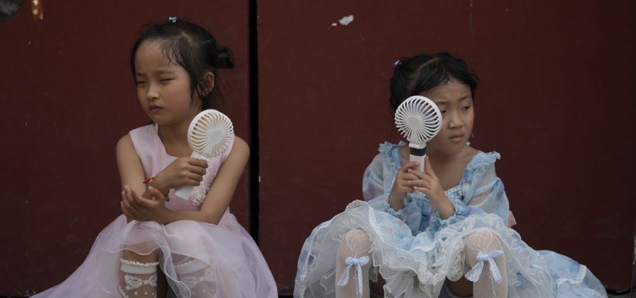Children cool themselves with electric fans in Beijing. They are wearing princess dresses.