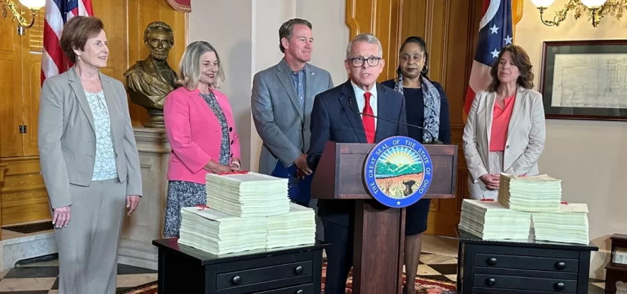 Ohio Gov. Mike DeWine (center, in red tie) speaks to reporters about signing the two-year state budget. Alongside him are (l-r): Ohio Medicaid Director Maureen Corcoran, Office of Budget and Management Director Kim Murnieks, Lt. Gov. Jon Husted, Ohio Department of Aging Director Ursel McElroy and Department of Mental Health and Addiction Services Director Lori Criss.