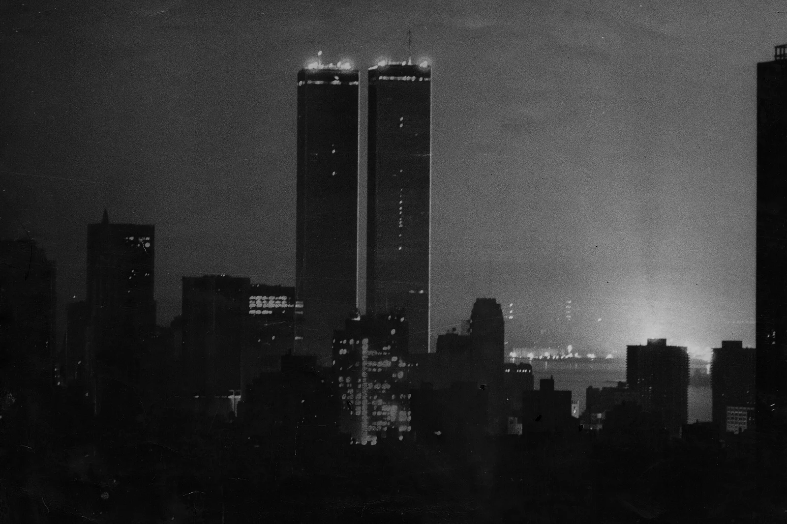 A black and white photo with the twin towers in NYC pictured against a night sky. 