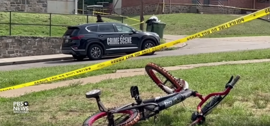 A bike rests under yellow caution tape with a police van in the background.