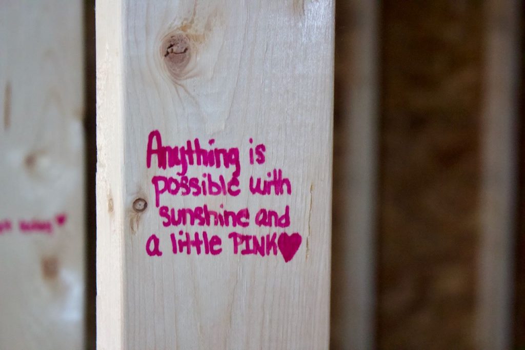 A wooden beam inside the house with the words "Anything is possible with sunshine and a little pink" written in hot pink Sharpie.