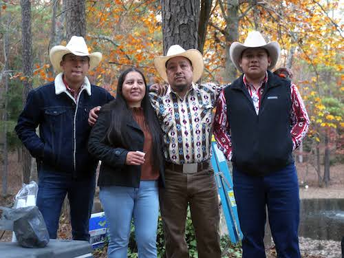 The Juárez Family, including Flaco, Cecilia, Tacho and Alan, stand with their arms around one another in front of a backdrop of trees, orange leaves, and a lake.