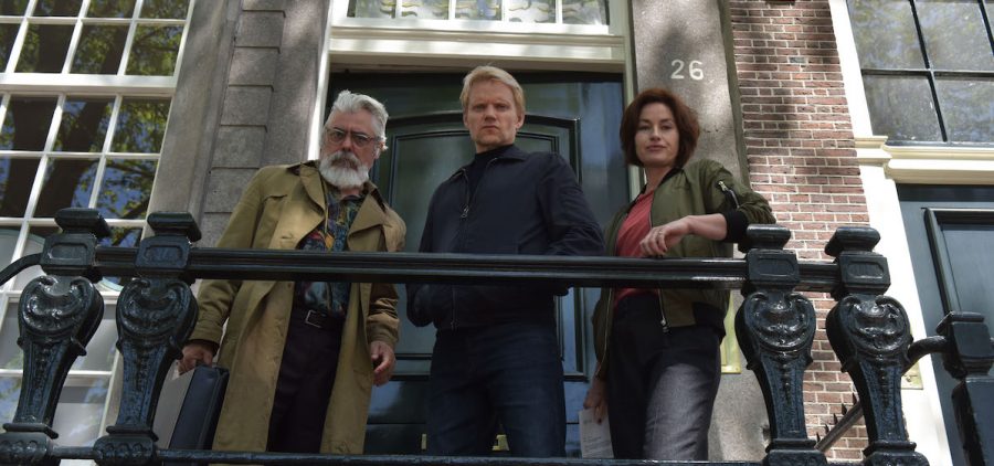 the cast of "Van der Valk" Season 3 standing on balcony, shot from below. "Van der Valk" Season 3