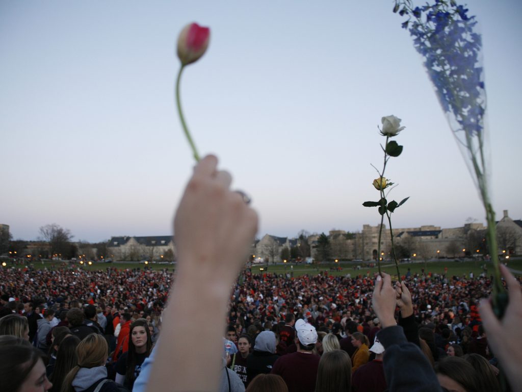 People gather for a vigil after the 2007 Virginia Tech shooting Blacksburg, Va. Several people hold up flowers.