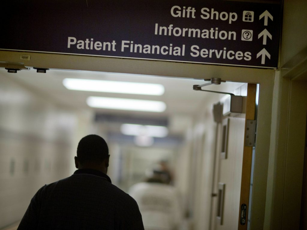 A person walks down a hospital hallway under signs that point to various parts of the hospital.