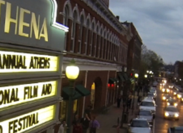 A photo of the exterior of the Athena Cinema taken in the nighttime. The photo is taken from the perspective of the marquee, which is lit up.