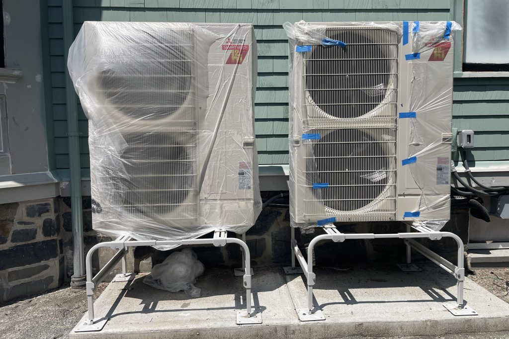 Heat pumps with plastic bags around them outside of a home.