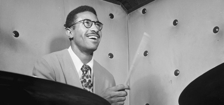 drummer Max Roach behind a barely visible drum set smiling while playing