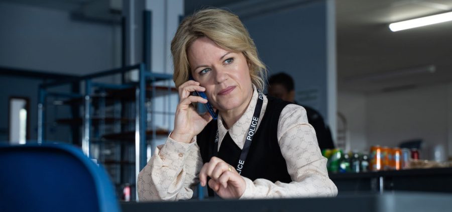 DCI Jess James (SINÉAD KEENAN) wearing a police lanyard, on the phone at her desk (C) Mainstreet Productions