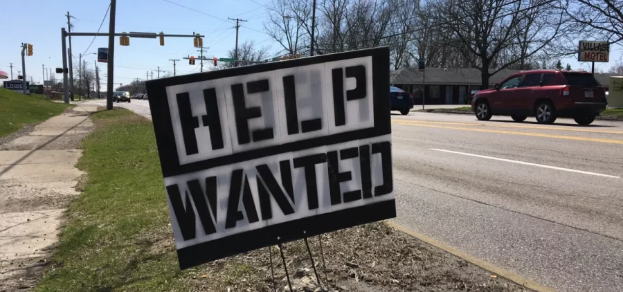 A black and white Help Wanted sign sits on the side of the road
