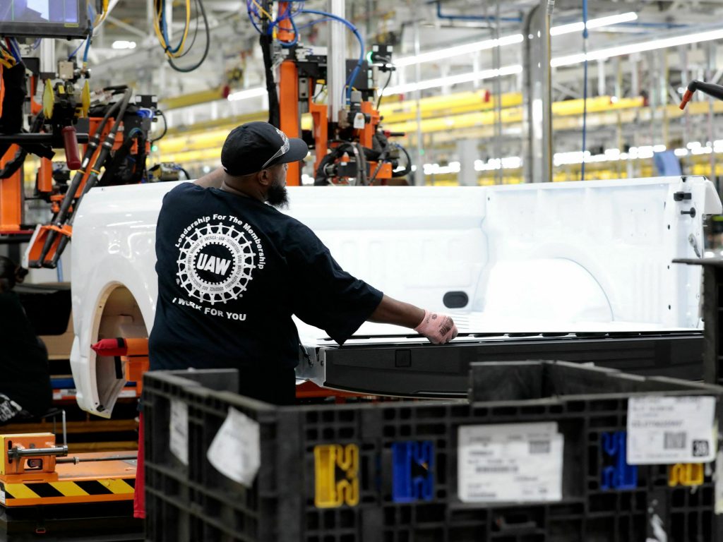 A man in a United Auto Workers shirt works on a Ford F-150 Lightning bed.
