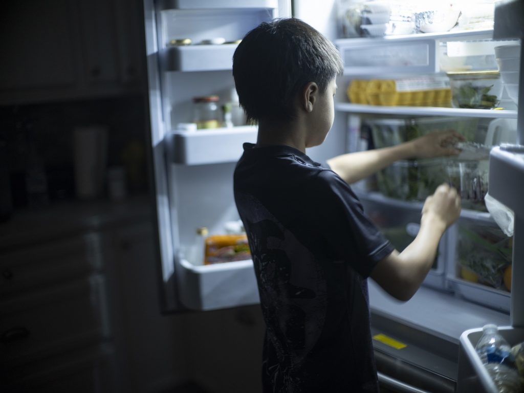A child reaches for something in a refrigerator.