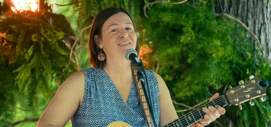 An image of Megan Bee performing for the 2023 Sycamore Sessions. She is wearing a blue sleeveless dress and holding a guitar.