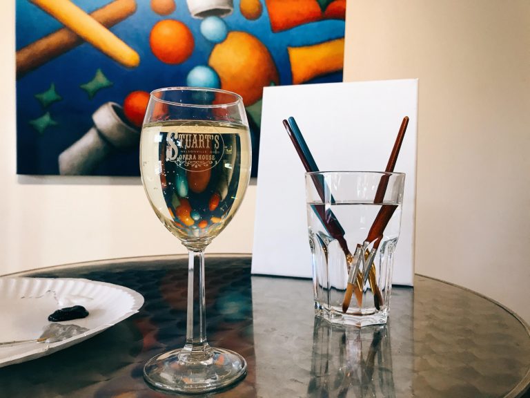 A picture of a glass of wine next to paintbrushes.