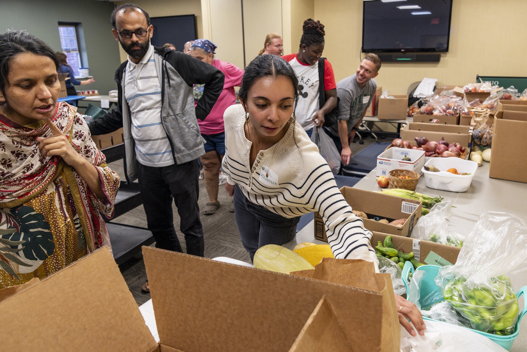 An image of people preparing food for a food bank. They are wearing gloves and packing boxes.