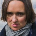 An press image for Sarah Vowell. She has short hair and is wearing a large scarf.