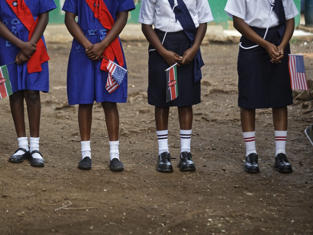 Girls hold U.S. and Kenyan flags while waiting for the arrival of a U.S. ambassador at a site supported by PEPFAR in Nairobi, Kenya 