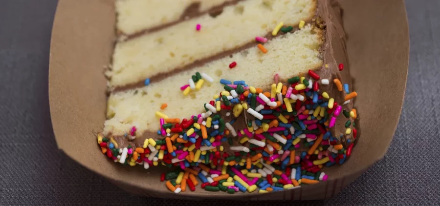 On a plate is a piece of cake with sprinkles on the top.