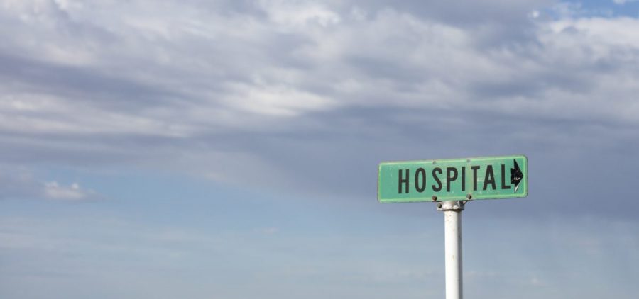 A hospital sign on a white pole on a rural road with nothing else around