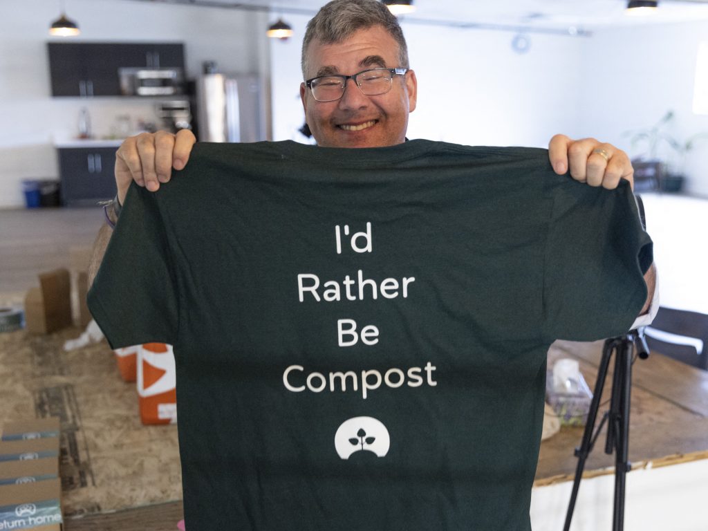 Return Home CEO Micah Truman holds up a T-shirt with a lighthearted slogan ("I'd rather be compost") during a tour of the Return Home funeral home