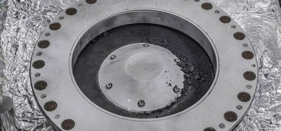 Small rocks and dust from an asteroid, outside a round sample collection device in a NASA lab.