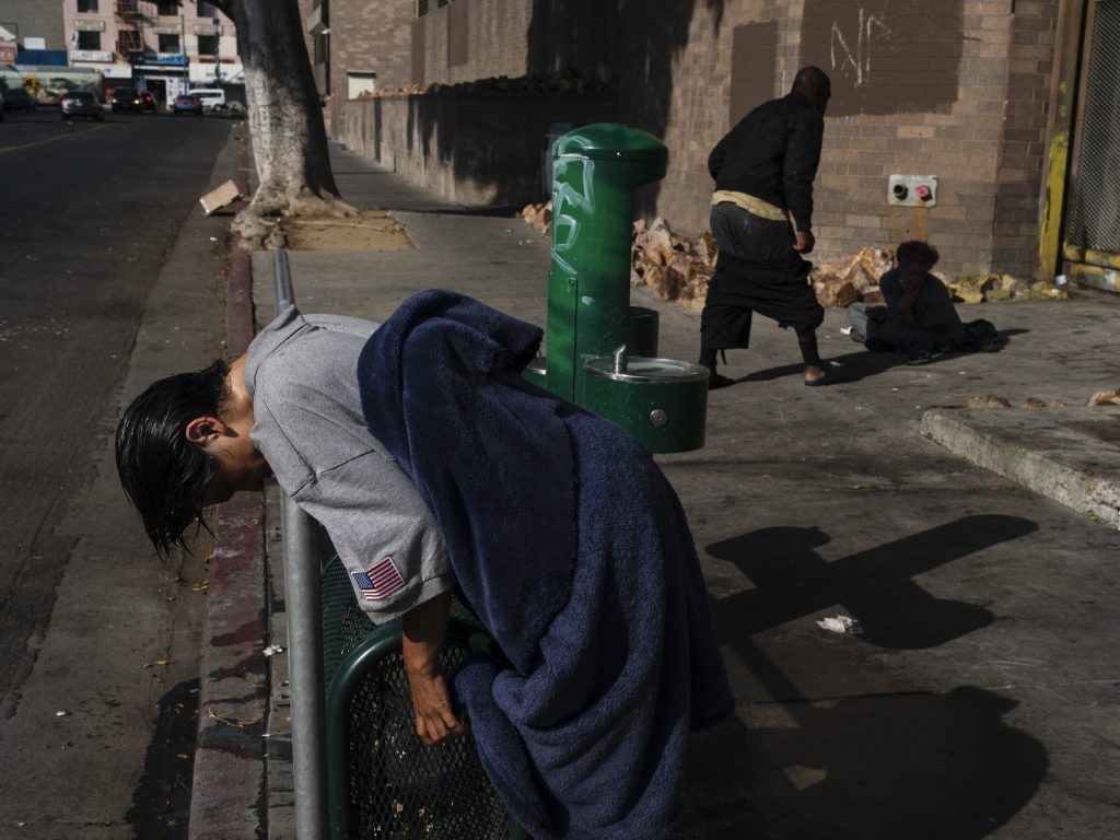 A mentally ill homeless woman leans on a rail after wetting her hair at a drinking fountain in the Skid Row area of Los Angeles,