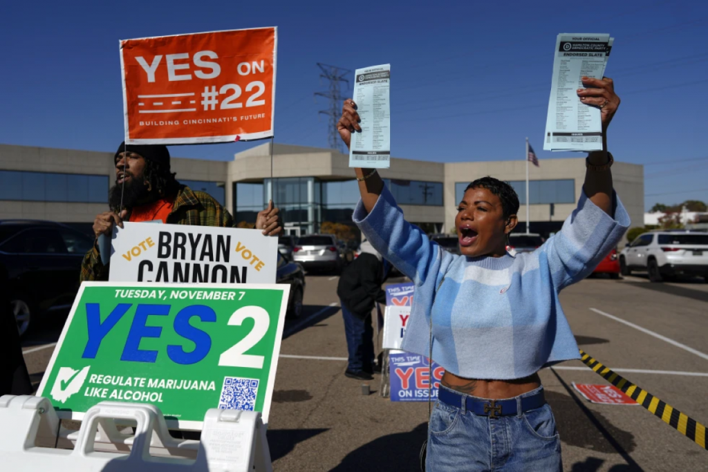 A woman holds out pamphlets promoting issue 2. She is surrounded with "Yes" signs for issue 2.