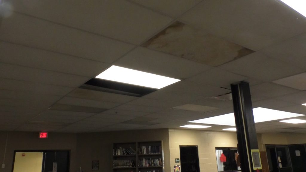 A photo of ceiling of the library at Athens High School with missing pieces and brown-stained parts from water leaks.
