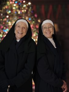 Two nuns, Sister Monica Joan (JUDY PARFITT) and Sister Juliene (JENNY AGUTTER)smiling in front of Christmas tree