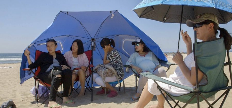 A group of expectant mothers sit on the beach under an umbrella.