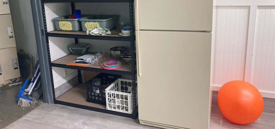 A refrigerator sits next to a shelf with dishware.