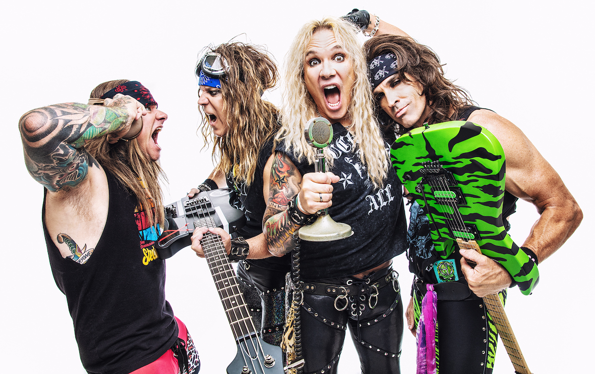 A promotional image of the band Steel Panther. All four members are posing against a white backdrop. 