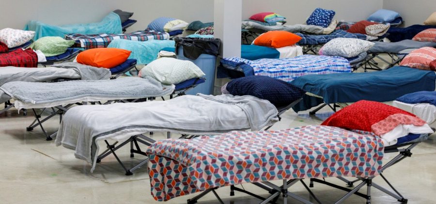 Rows of cots with blankets and pillows in a large open facility.