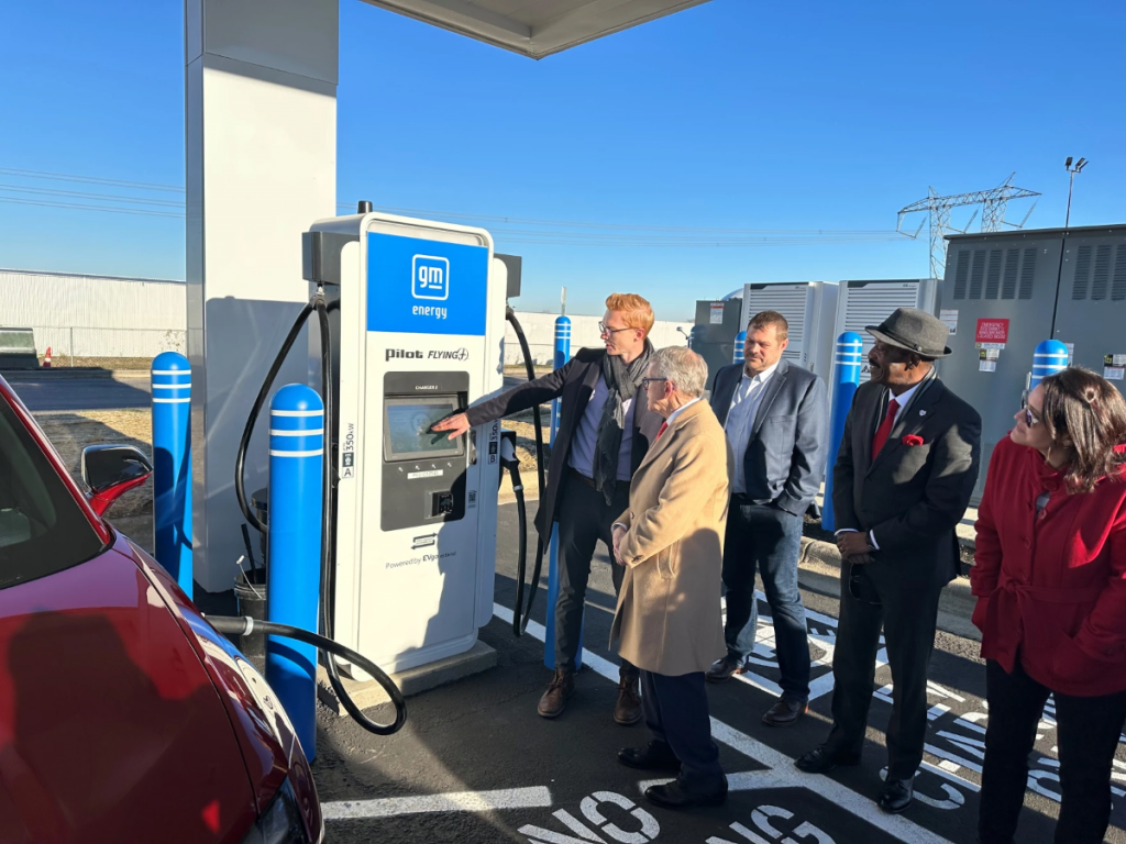 Governor Mike DeWine stands with a small crowd watching a man showing off the new charging station.