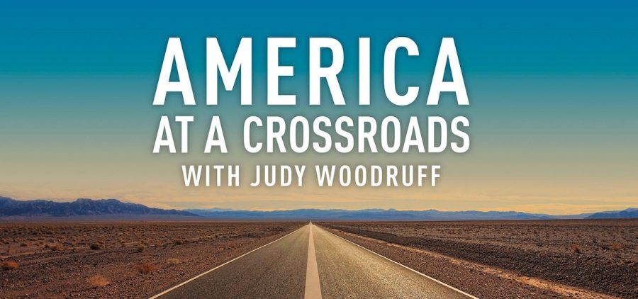 desert picture of long straight road, mountains on the horizon. Title slide for America At A Crossroads with Judy Woodruff