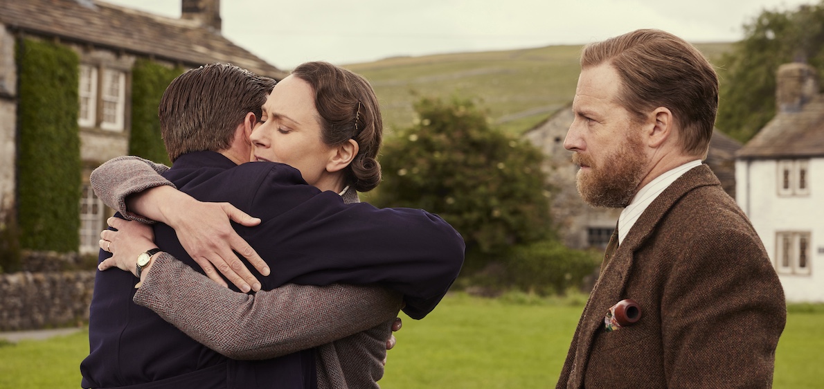 Shown from left to right: Nicholas Ralph as James Herriot, Anna Madeley as Mrs. Hall and Samuel West as Siegfried Farnon. Hames and Anna embrace as Siegfried looks on. Courtesy of Playground Entertainment and MASTERPIECE