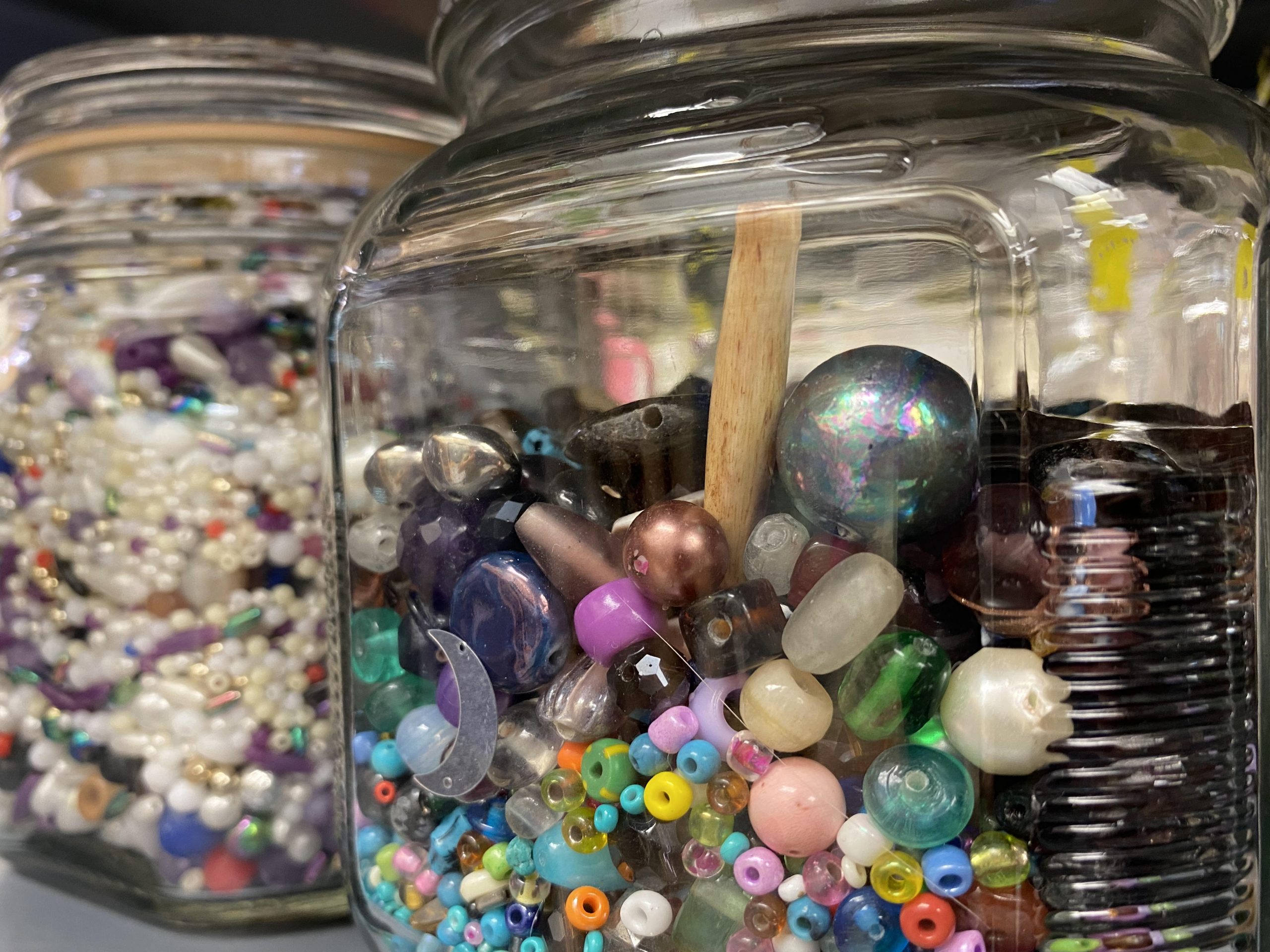 A close up of beads in a clear glass jar.