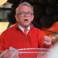 Gov. Mike DeWine at a clear podium speaking to a crowd in Cincinnati.