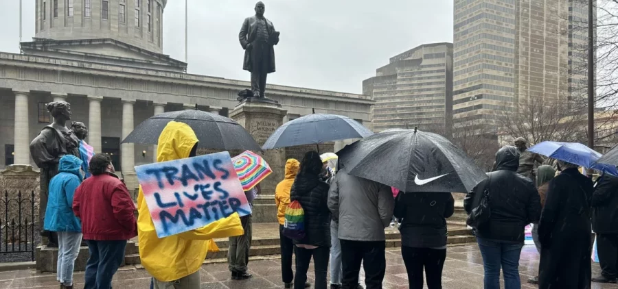 LGBTQ activists stand in the rain outside the Ohio Statehouse as the Senate debates overriding Gov. Mike DeWine‘s veto of House Bill 68