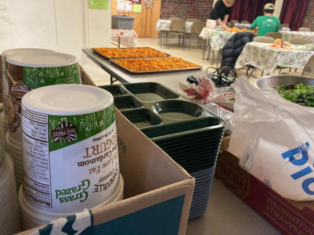 Food trays, Snowville yogurt containers, and trays of chopped butternut squash sit out in preparation for a free meal program.