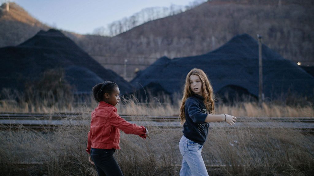An image of two young girls walking together with mountains in the background. 