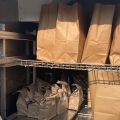 A woman wearing a medical mask stands beside paper bags with meal deliveries for the program Meals on Wheels.