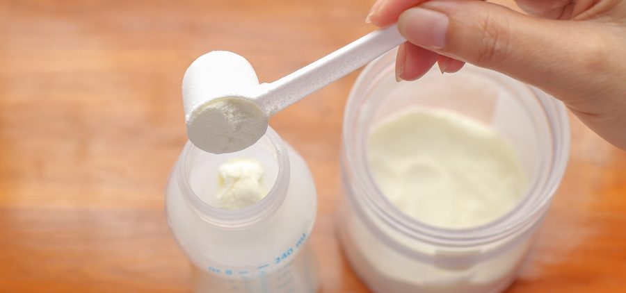A person puts powdered milk into a baby bottle.