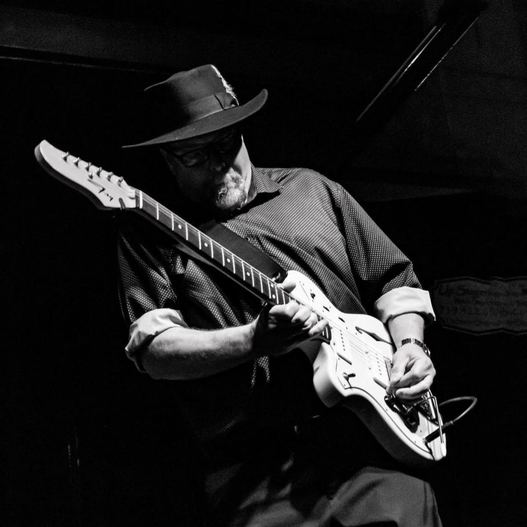 A promotional image of blues musician Tom Holland. It is in black and white and he is playing a guitar. 