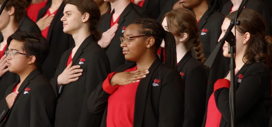Chicago Childrens Choir in performance. All wearing red shirts and black jackets. All students have their hand over their heart. Photo: IronZeal Films