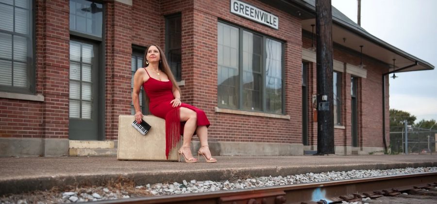A promotional image of Eden Brent. She is sitting at a train station by herself in a red dress.